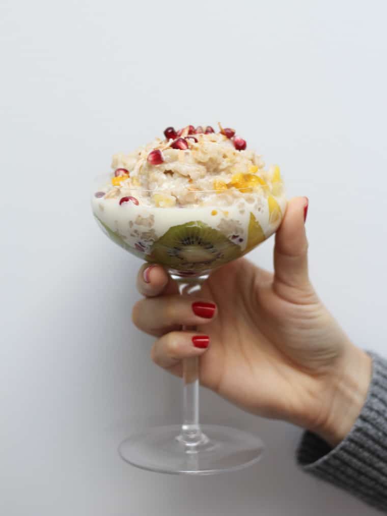 A glass of rice pudding with kiwi and mango being held up.