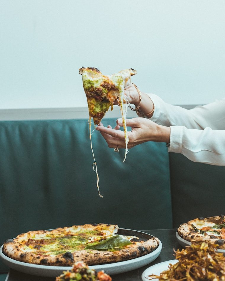 Person taking a cheesy slice of pizza from a pie.