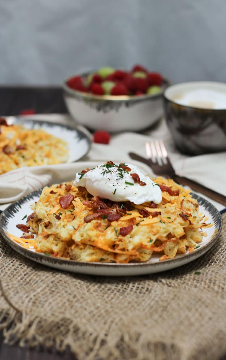 A plate of a loaded potato waffles with an egg on top on a plate.