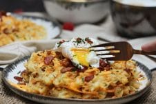 A plate of a loaded potato waffles with an egg on top with a fork cutting in.