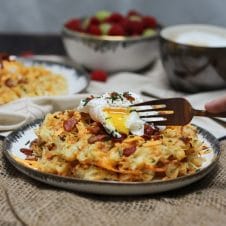 A plate of a loaded potato waffles with an egg on top with a fork cutting in.