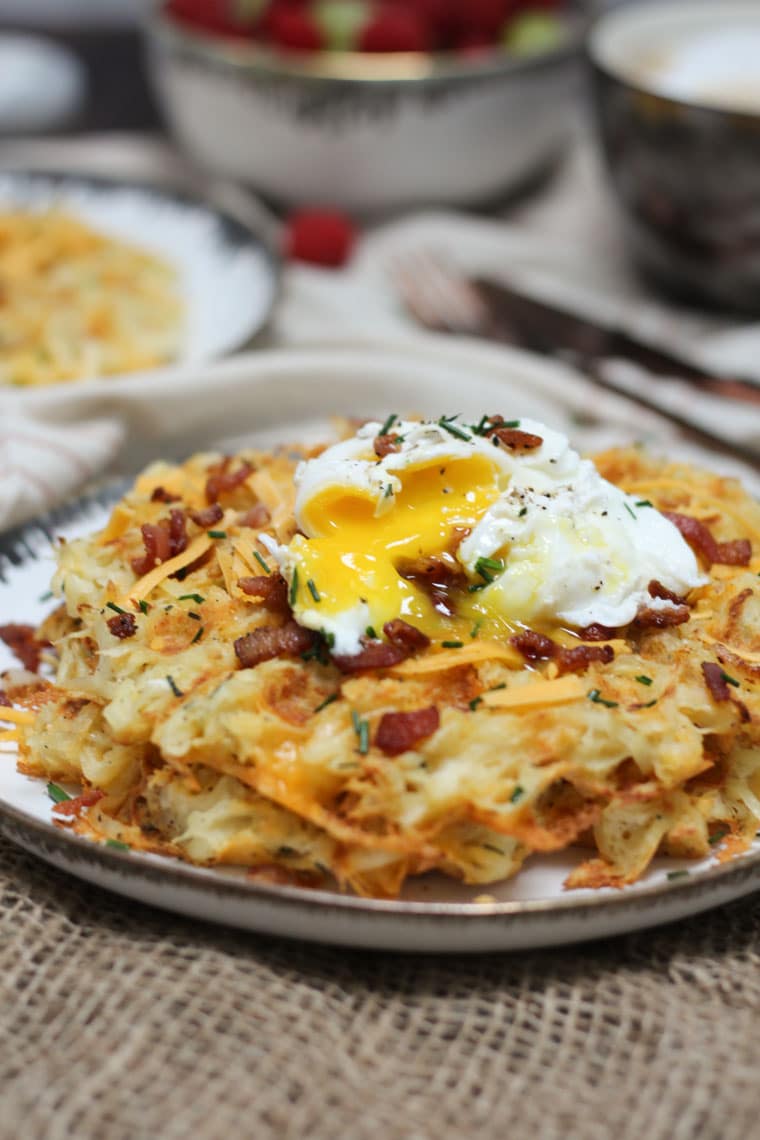 A plate of a loaded potato waffles with an egg and bacon crumbles on top.
