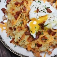 A plate of a loaded potato waffles with an egg on top.