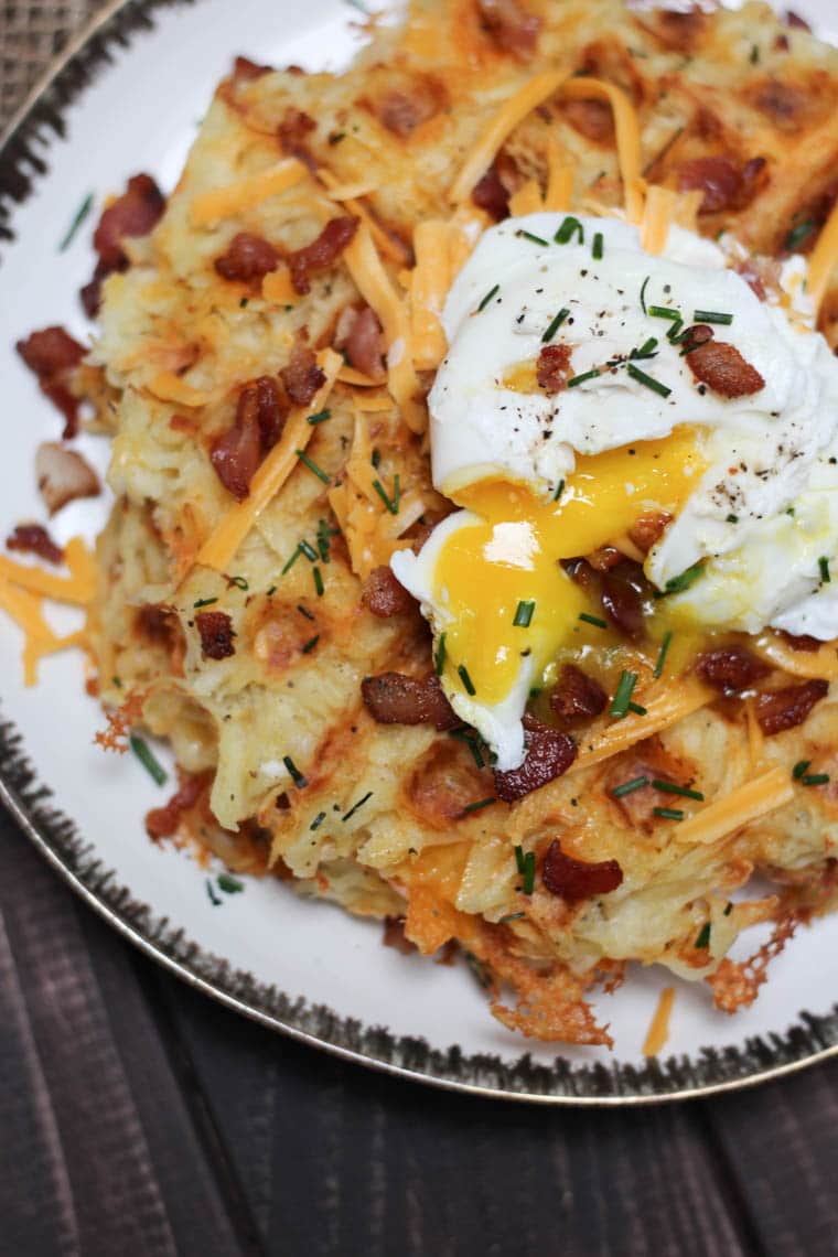 A plate of a loaded potato waffles with an egg on top.