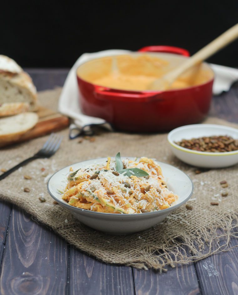 gluten free pumpkin zoodles in a white bowl topped with pumpkin seeds, herbs, and cheese