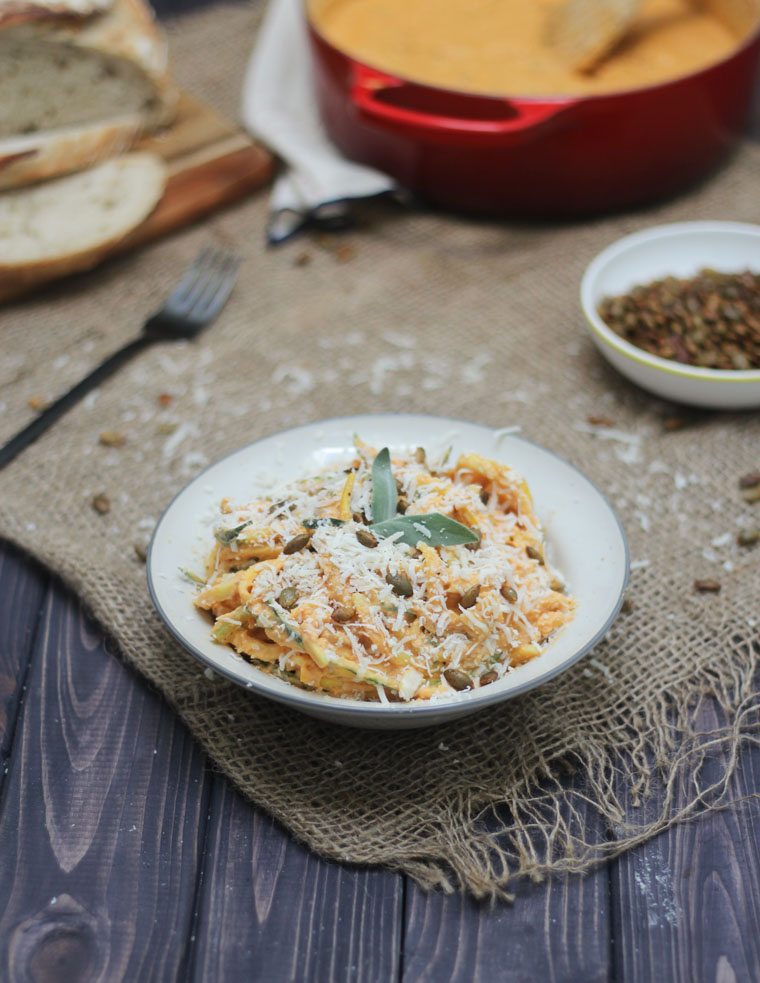 keto pumpkin zoodles in a white bowl garnished with herbs, cheese, and pumpkin seeds