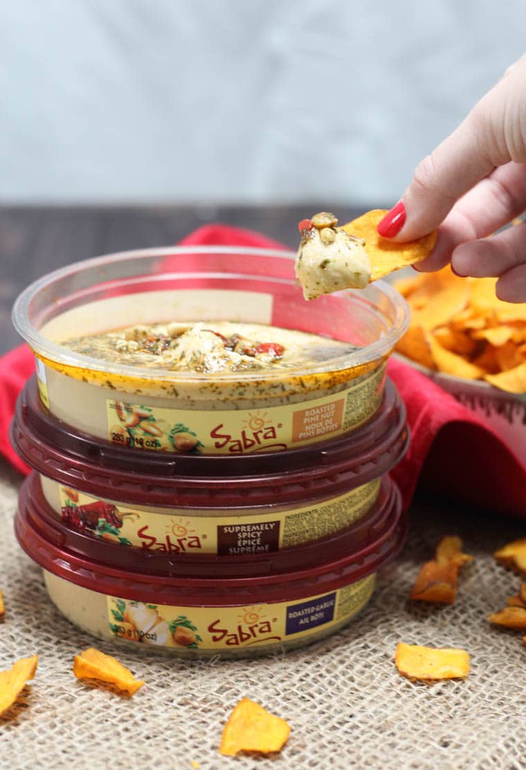 A stack of three sabra hummus with a chip being dipping into one.