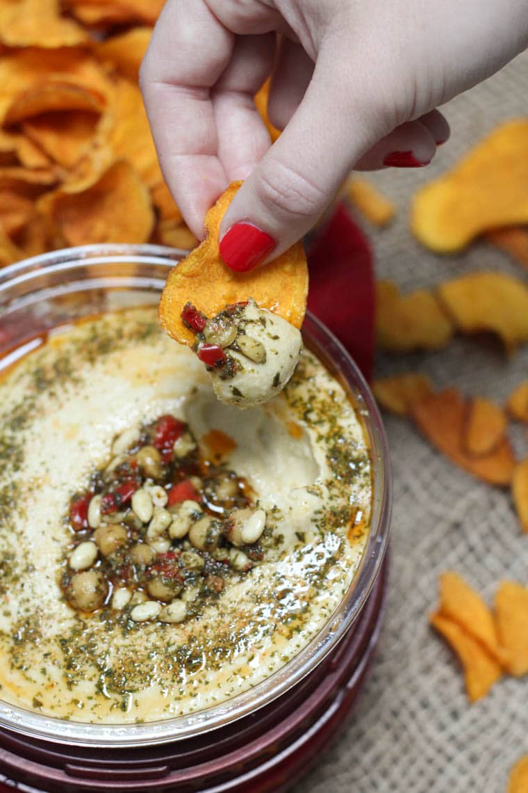 A container of hummus with a chip being dipped in.