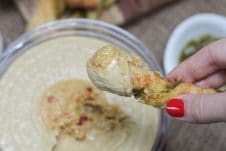 A pesto pizza twist being dipped into hummus.