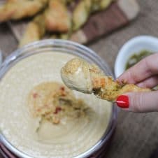 A pesto pizza twist being dipped into hummus.