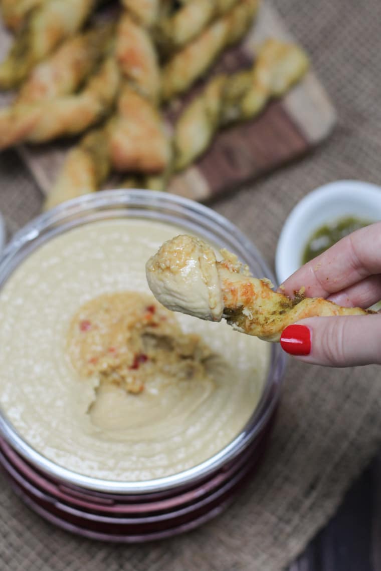 A pesto pizza twist being dipped into hummus.