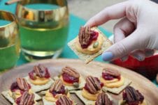 A plate of sweet potato and cranberry mousse bites with a hand lifting up a single one and two glasses in the background.