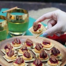 A plate of sweet potato and cranberry mousse bites with a hand lifting up a single one and two glasses in the background.