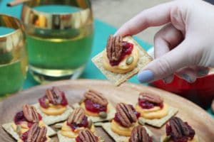 A plate of sweet potato and cranberry mousse bites with a hand lifting up a single one and two glasses in the background.