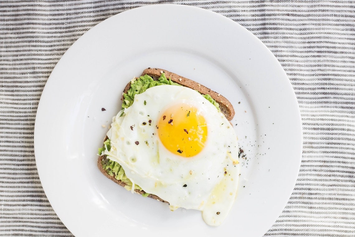 birds eye view of an egg on top of avocado toast on a white plate