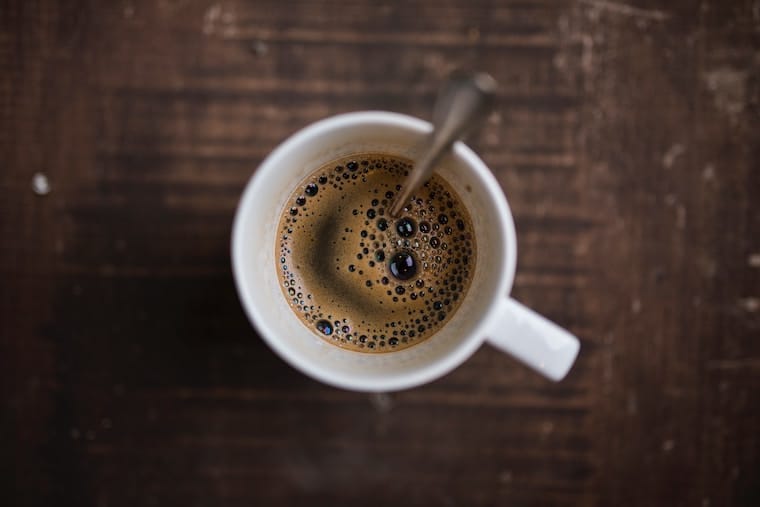 Birds eye view of coffee in a mug with a stir spoon as a cause for stomach cramps. 