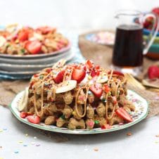 A stack of birthday cake protein waffles on a white plate with strawberries on top.