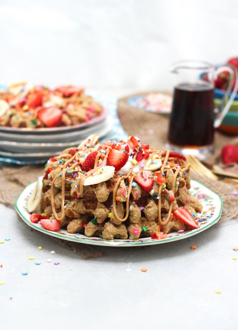 A stack of birthday cake protein waffles on a white plate with strawberries on top.