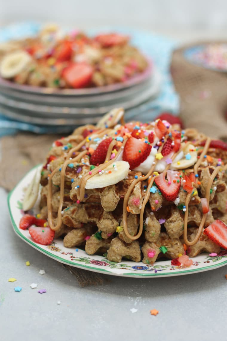 A stack of birthday cake protein waffles on a white plate with strawberries and sprinkles on top.