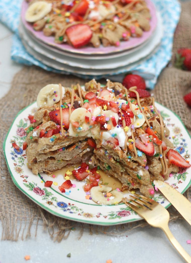 A stack of birthday cake protein waffles on a white plate with strawberries on top cut opened.