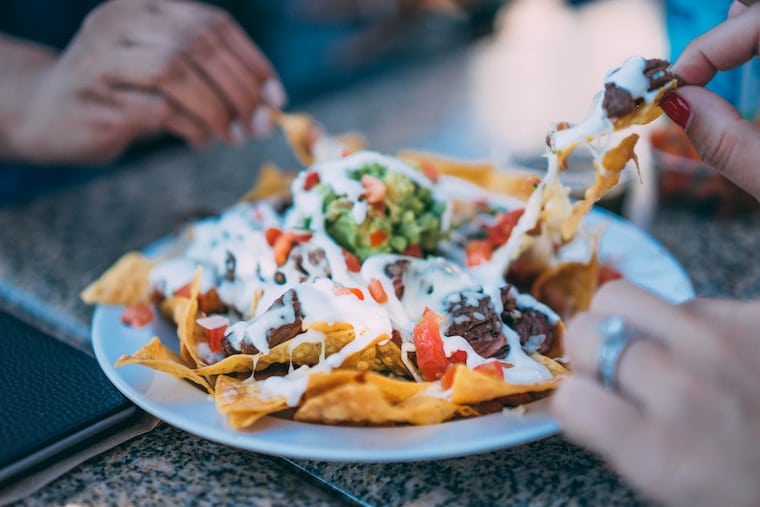 multiple hands reaching for a plate of nachos