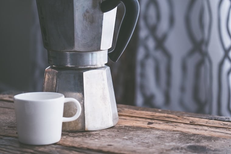 coffee maker next to a white mug on a wooden counter