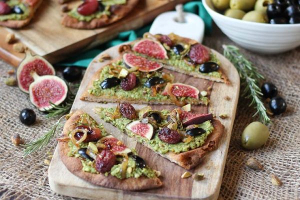 Vegan Olive Pesto Flatbread with Olives from Spain, Roasted Grapes and Figs This Vegan Olive Pesto Flatbread with Olives from Spain, Roasted Grapes and Figs is a perfect plant-based healthy holiday appetizer to feed a crowd! Serves 16 Gordal olives from Spain Pesto 1/2 cup pistachios (shelled) 1 cup pitted Gordal olives from Spain 1 garlic clove, minced 1 cup arugula ¼ cup extra virgin olive oil Pepper, to taste Flatbread 3 tbsp extra virgin olive oil, divided ½ onion, thinly sliced 1 ½ cups red grapes 2 sprigs rosemary 6 small whole grain naan breads 4 figs, thinly sliced ¼ cup pitted Dark Hojiblanca olives from Spain, thinly sliced ¼ cup crushed pistachios In a food processor, puree the pistachios until they reach a powder like consistency, then add in the Gordal olives from Spain, garlic, arugula and oil. Season with pepper, to taste. Set aside. Preheat oven to 450 F. Heat a tablespoon of oil in a nonstick skillet over medium-low heat. Add in the onions and saute until dark and caramelized, about 50 minutes. Set aside. Meanwhile, place the grapes and rosemary on a baking sheet and drizzle with a tablespoon of oil. Place the naans on baking sheets and drizzle with the remaining tablespoon of oil. Roast the grapes for 20-25 minutes or until caramelized, and the flatbread for 5-10 minutes just until toasted around the edges. When ready to serve, smear the olive pesto all along the toasted naans. Top with the roasted grapes, figs, Dark Hojiblanca olives from Spain, caramelized onions and pistachios. Enjoy!