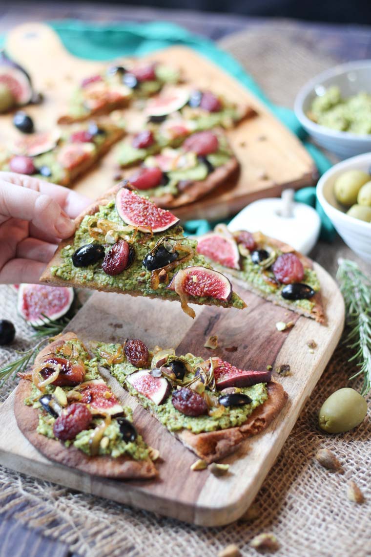 close up of a slice of vegan st. patrick's themed pesto olive flatbread with additional flatbread pieces on wooden serving boards in the background