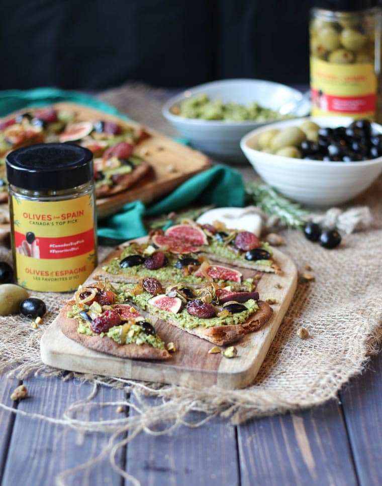 vegan pesto flatbread on a wooden serving board next jars of ilves