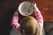 A girl sitting with a bowl of milk and cereal.