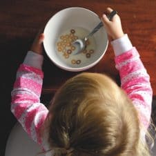 A girl sitting with a bowl of milk and cereal.