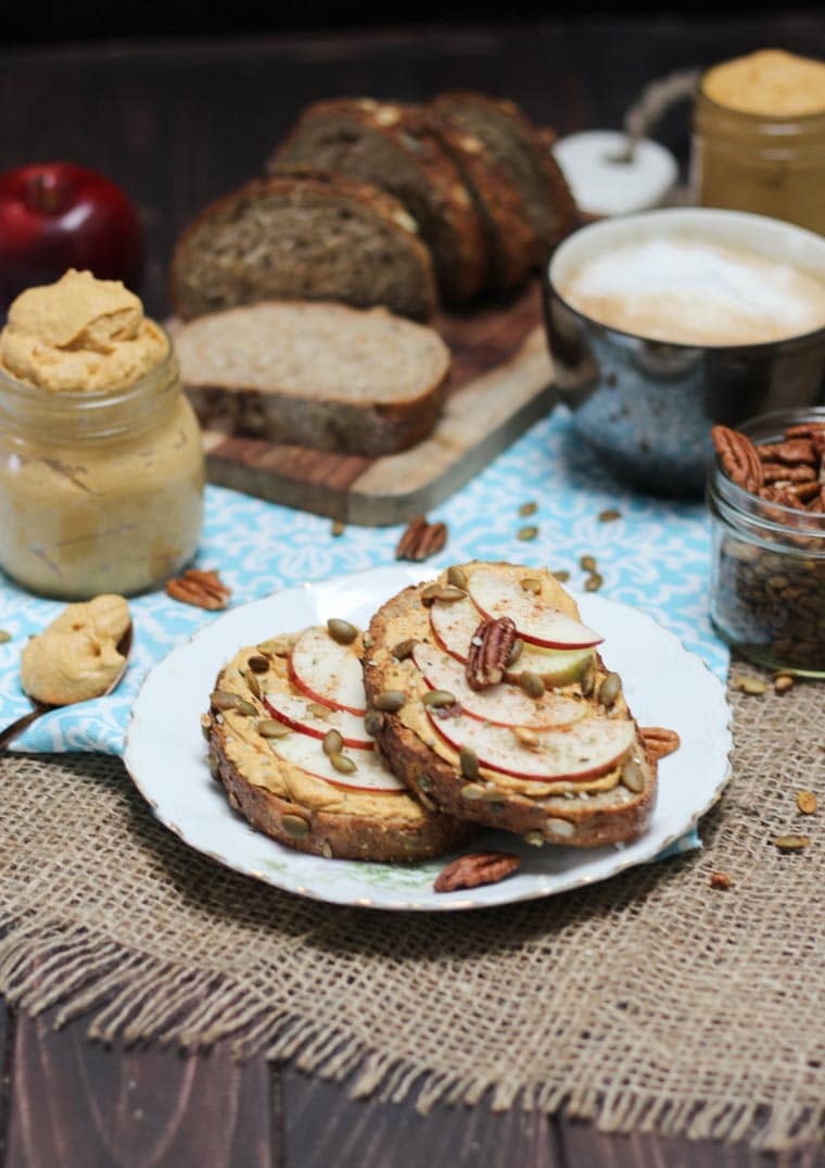 A plate with two pieces of toast with pumpkin pie butter spread on and topped with sliced apples and nuts.