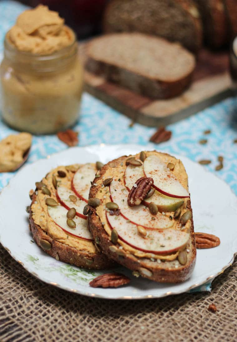 A close up of plate with two pieces of toast with pumpkin pie butter spread on and topped with sliced apples and nuts.