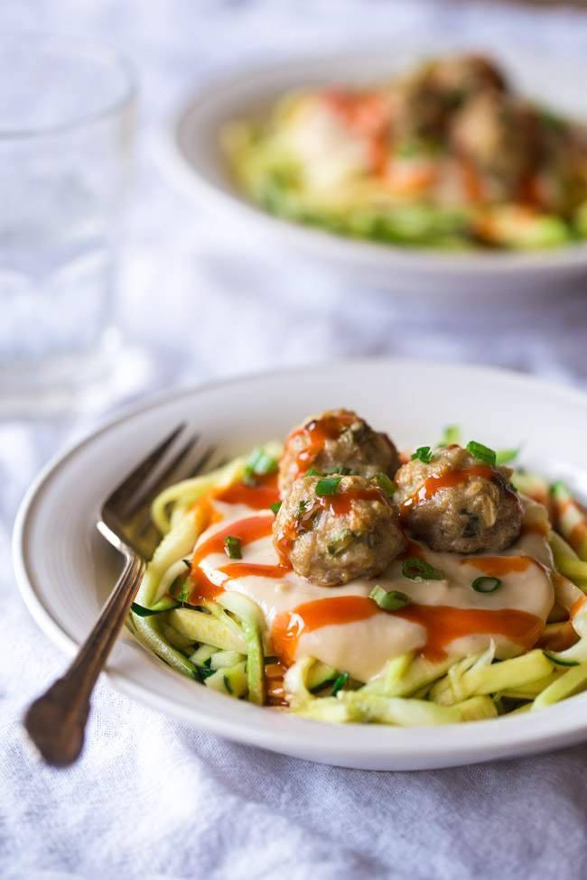 close up image of ranch buffalo meatballs over a bed of zucchini pasta garnished with fresh herbs in a white bowl