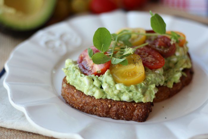 high protein avocado smash on toast garnished with tomatoes and greens on a white plate