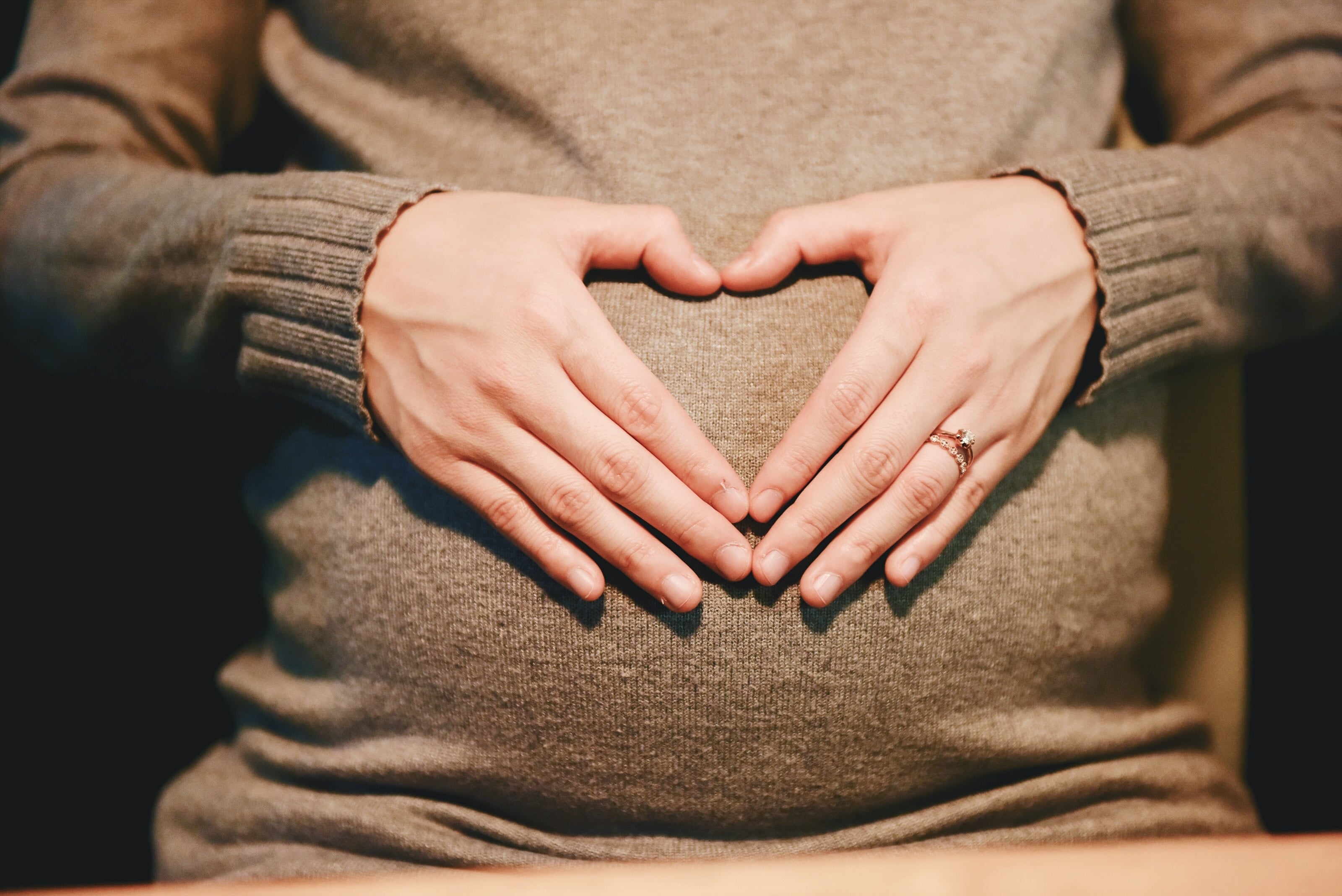 Hand making a heart over a pregnant stomach.