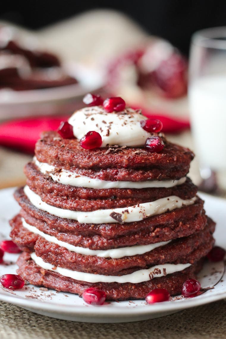 close up of stack of vegan red velvet protein pancakes garnished with chocolate and fruit on a white dish