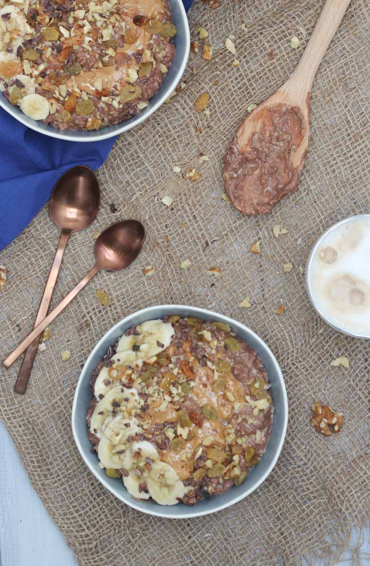 An overhead photo of a bowl of chocolate zucchini bread oatmeal zoats with bananas and chocolate chips on top with spoons around it.