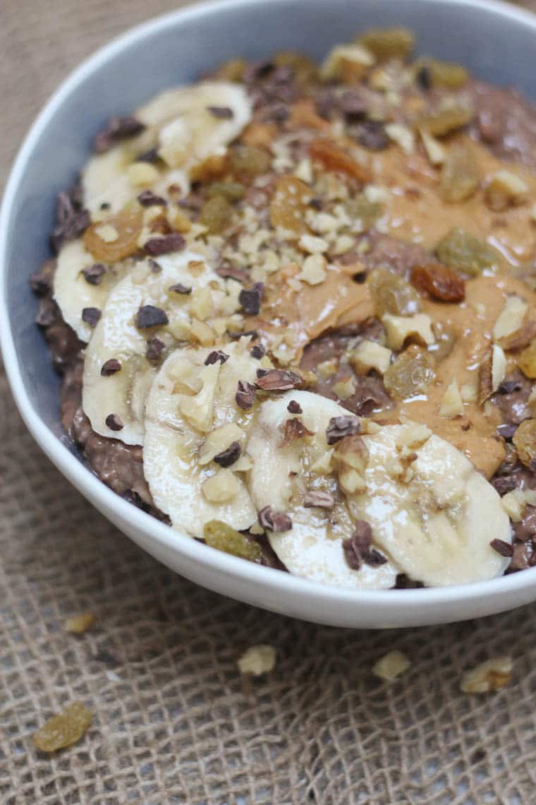 A close up photo of a bowl of chocolate zucchini bread oatmeal zoats with bananas and chocolate chips on top.
