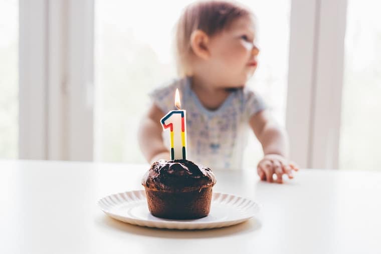 A baby sitting in front of a cupcake with a one year old candle.