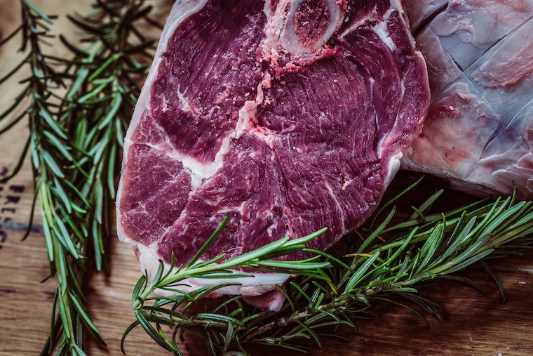 A close up of a raw steak with thyme around it.
