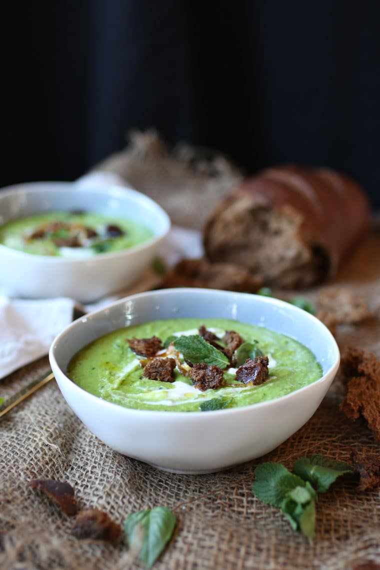 A white bowl with pea, mint, and coconut soup in focus with a second bowl in the background.