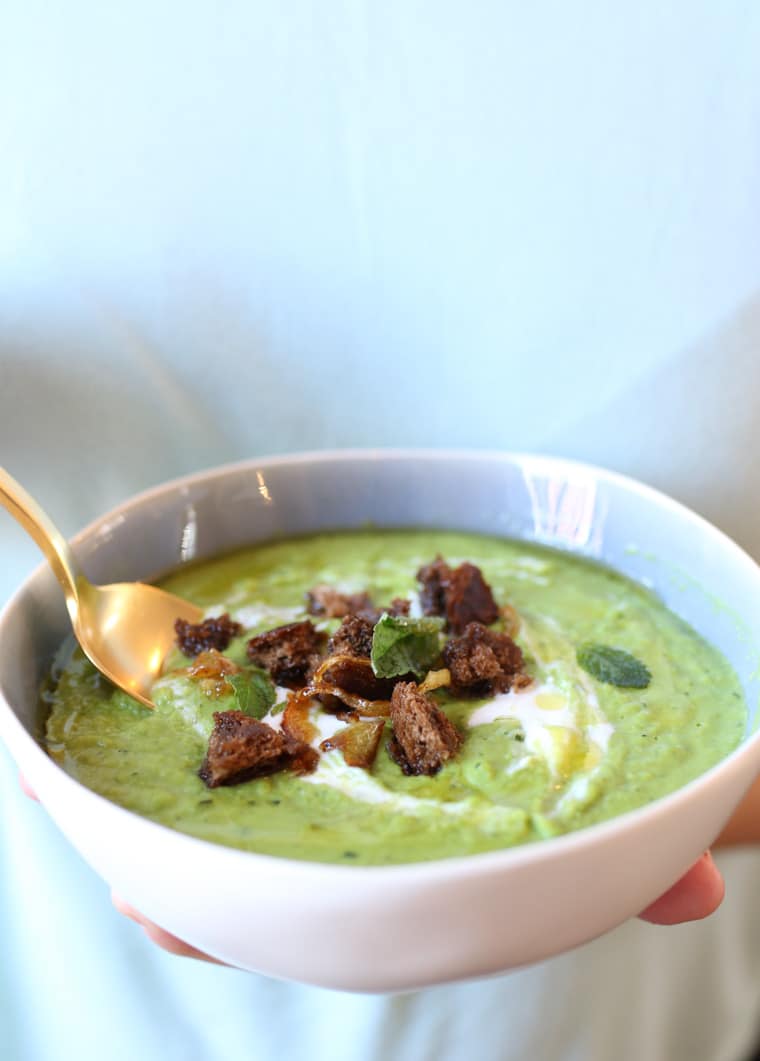A white bowl with pea, mint, and coconut soup with a spoon inside.