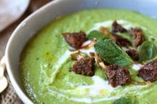 A close up image of a white bowl with pea, mint, and coconut soup.