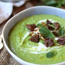 A close up image of a white bowl with pea, mint, and coconut soup.