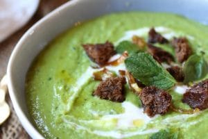 A close up image of a white bowl with pea, mint, and coconut soup.