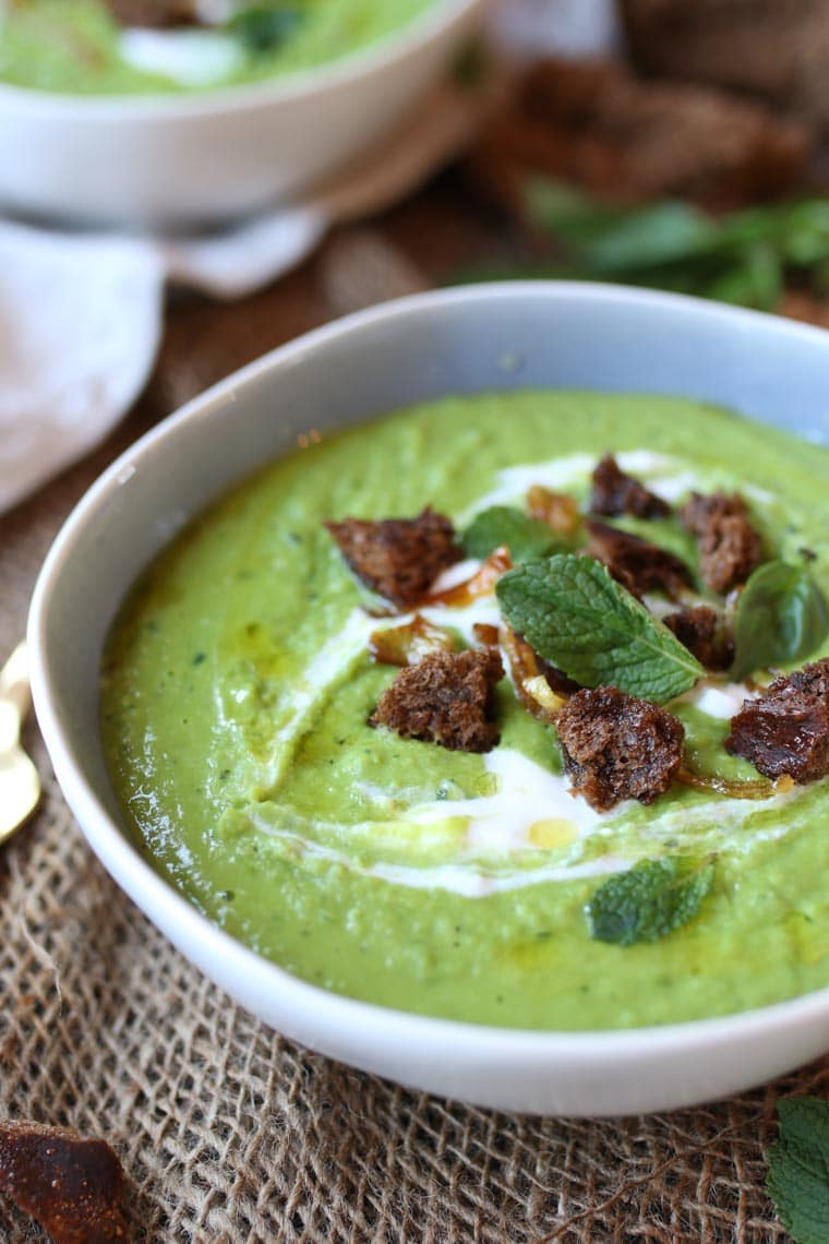 A close up image of a white bowl with pea, mint, and coconut soup.