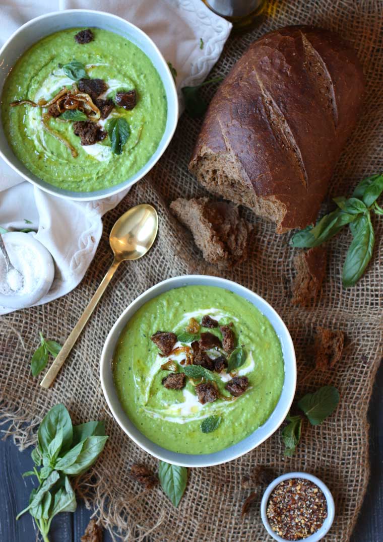 An overhead image of two white bowls with pea, mint, and coconut soup.