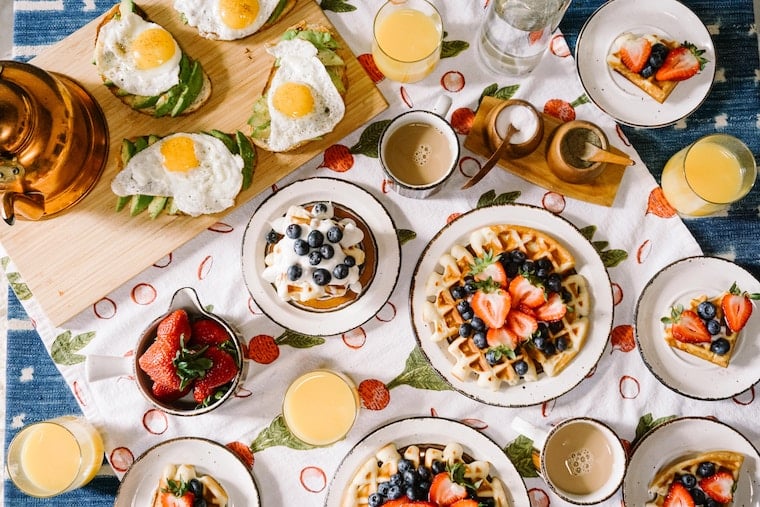An overhead photo of a brunch spread with waffles, eggs on avocado toast, and fruit.