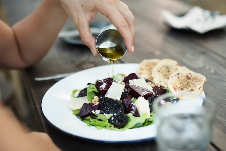 person pouring dressing over a salad in w hite bowl